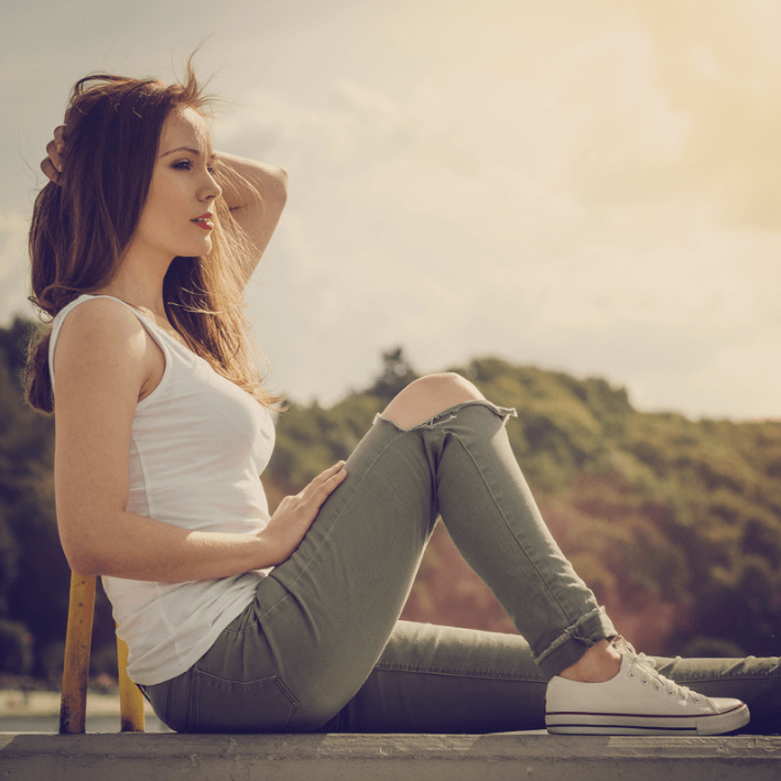 Woman sitting outdoors in casual attire, enjoying a sunny day, relaxed and stylish.