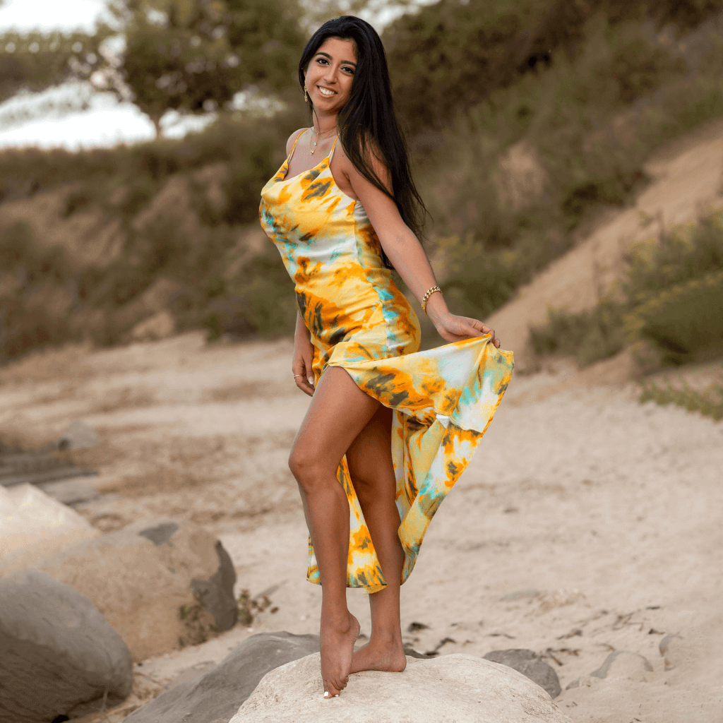 Woman in a colorful yellow and blue dress, playfully lifting her skirt on a sandy beach.