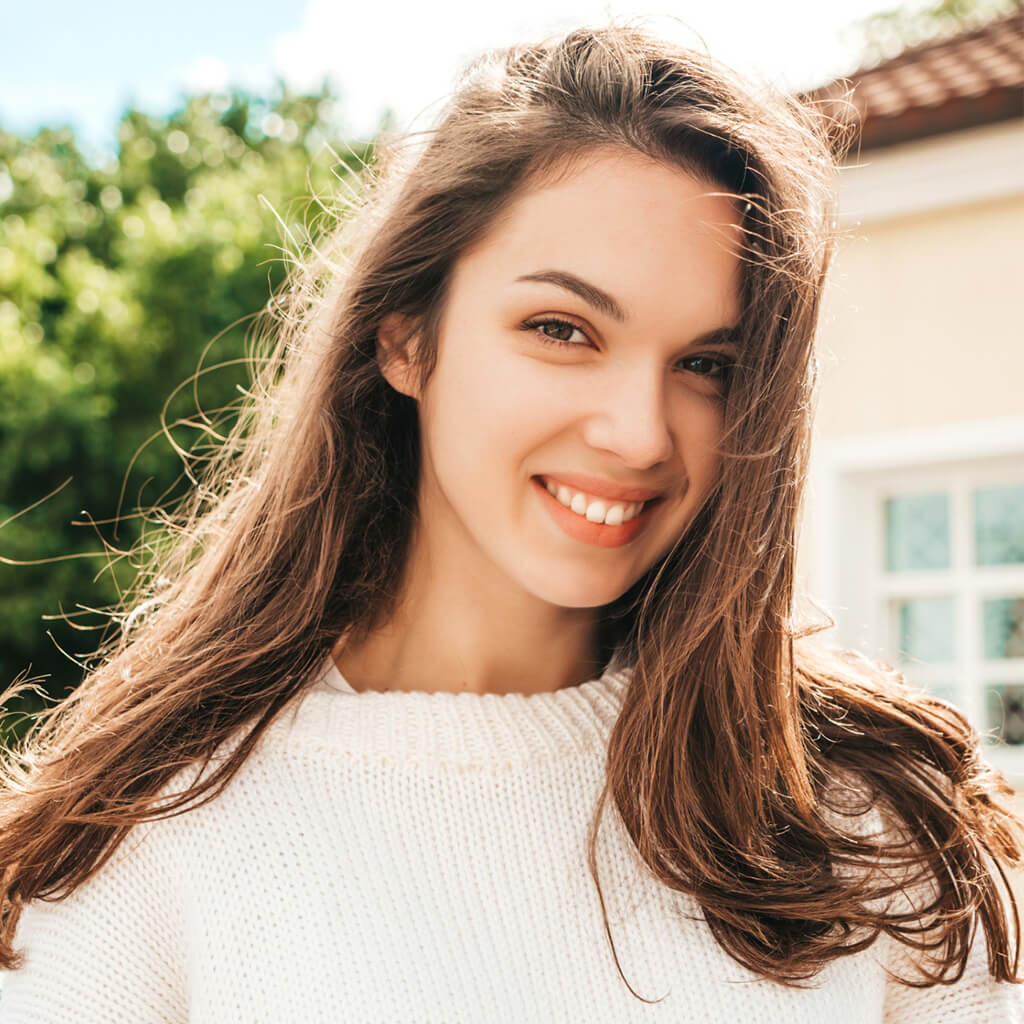 Smiling young woman with long hair in a white sweater, showcasing a radiant and polished look with Japanese Nano Refreshing Liquid.